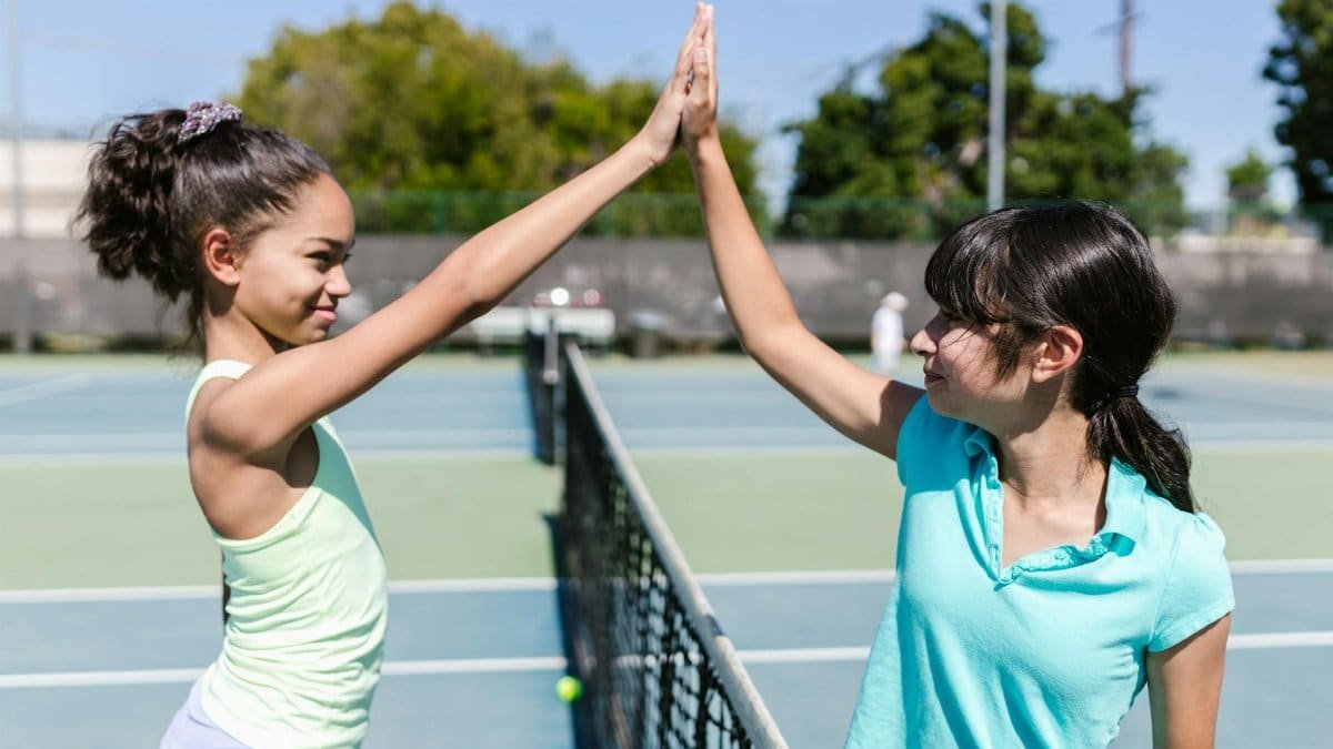 Two teenage girls enjoying a tennis match, high-fiving on an outdoor court.