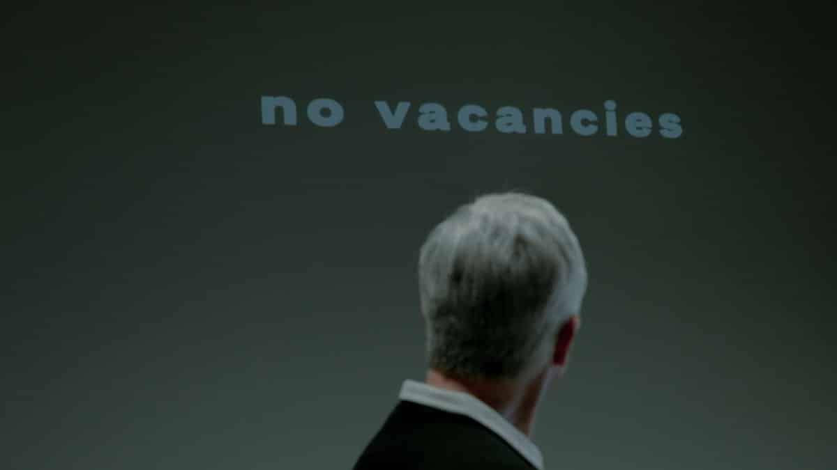 Senior man facing a 'No Vacancies' sign symbolizing job search challenges and ageism.