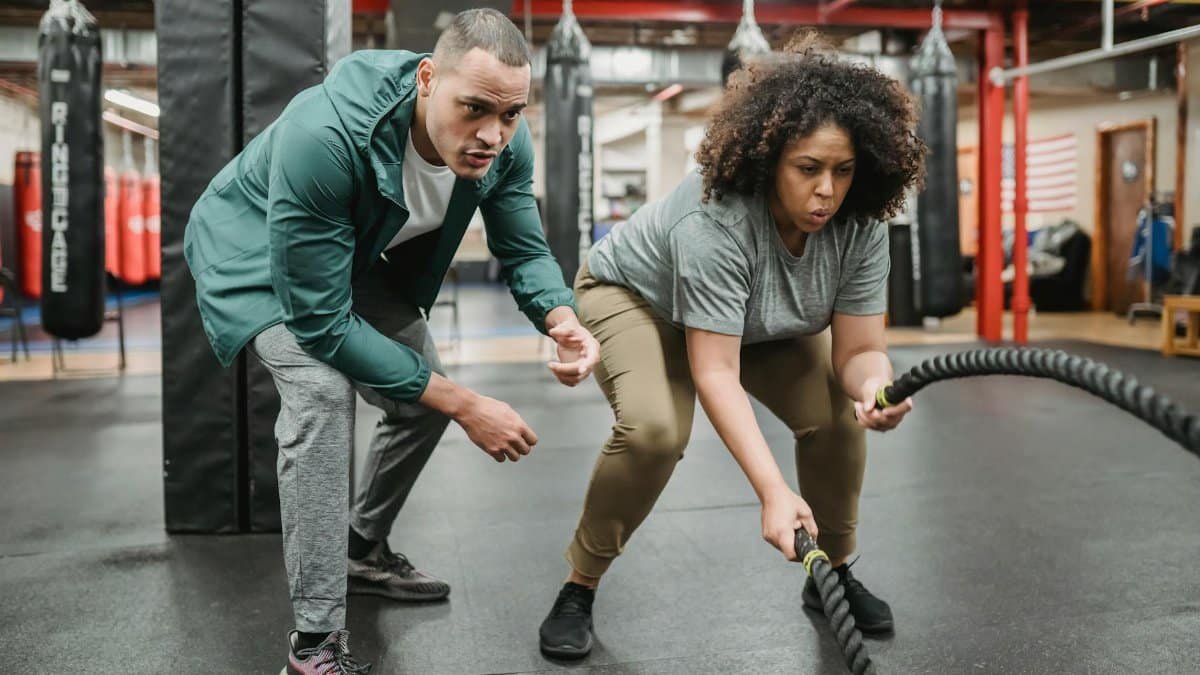 A dedicated woman focuses on battle rope training, guided by her fitness coach.