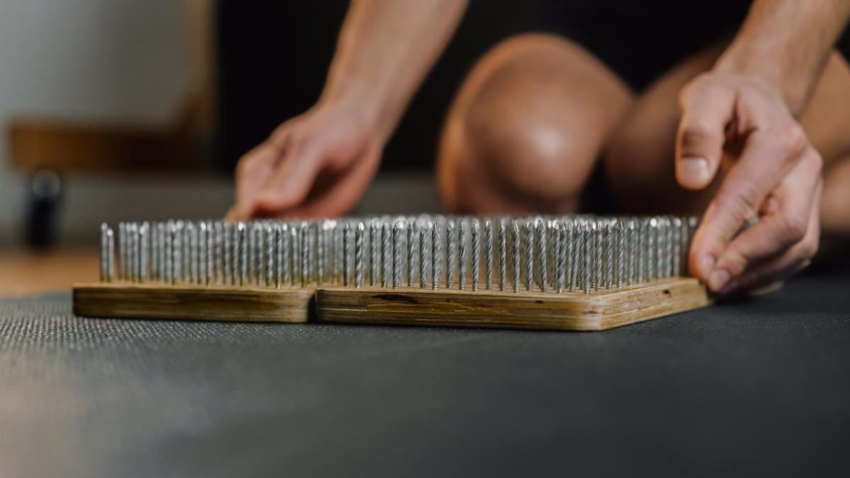Close-up of hands handling a wooden bed of nails, used for meditation or exercise.