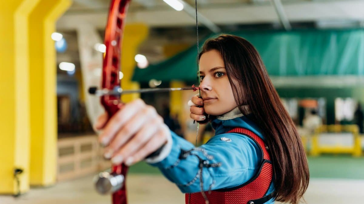 Young woman practicing archery indoors, showcasing skill and determination.