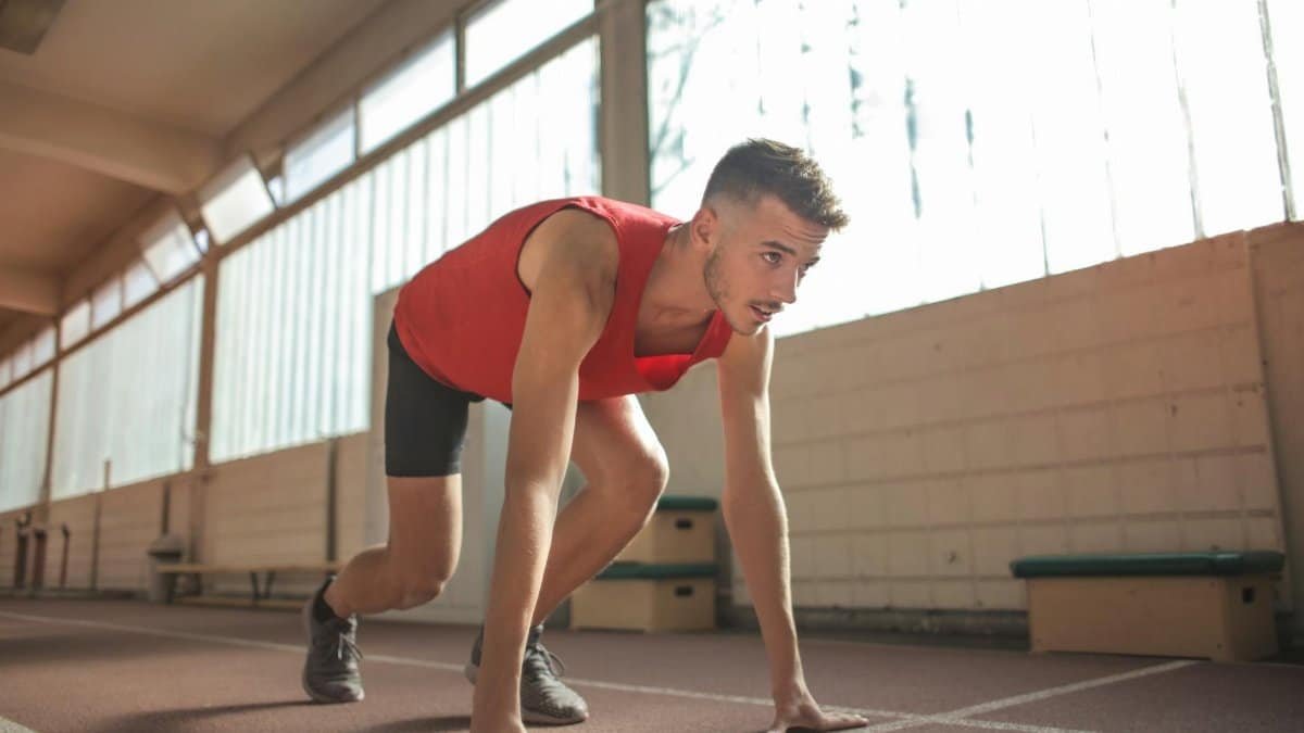 Focused male athlete in starting position indoors, ready to sprint.