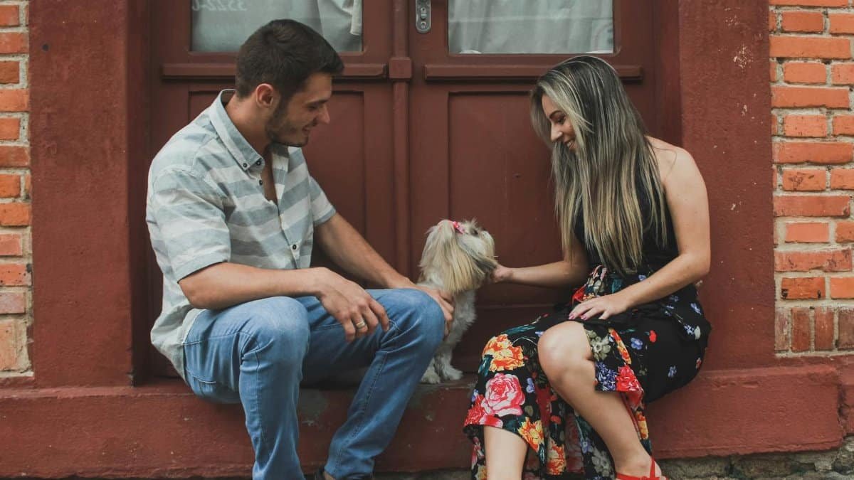 A couple sitting on a brick street smiling at their Shih Tzu dog.