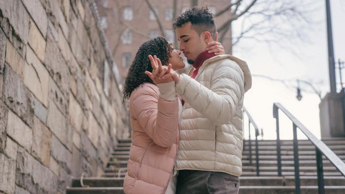 A loving couple in warm jackets embraces on a city staircase, creating a romantic moment.