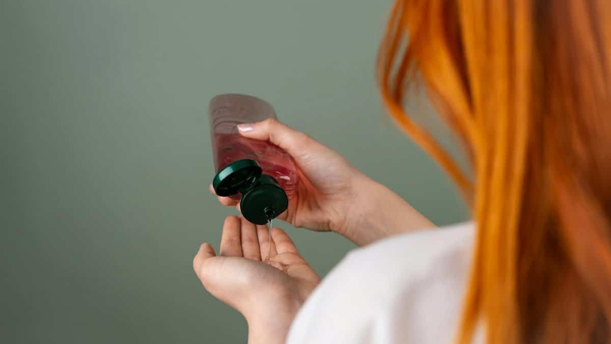 Woman pressing shampoo from a bottle into her hand, highlighting hair care routine.
