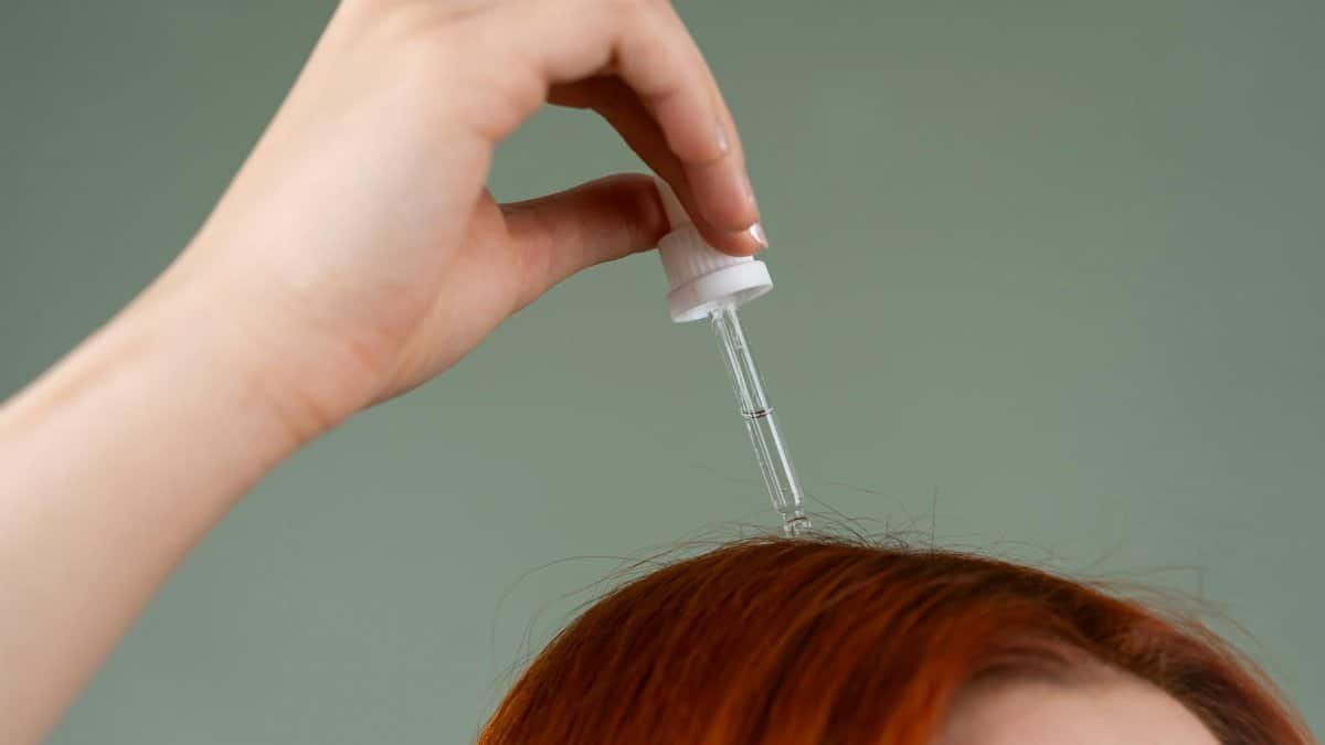 Close-up of hand applying hair serum on red hair with a dropper.