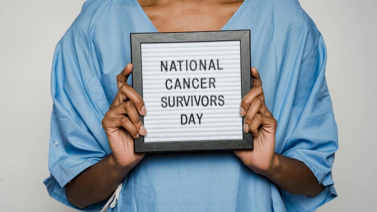 A person in a blue gown holds a sign marking National Cancer Survivors Day.