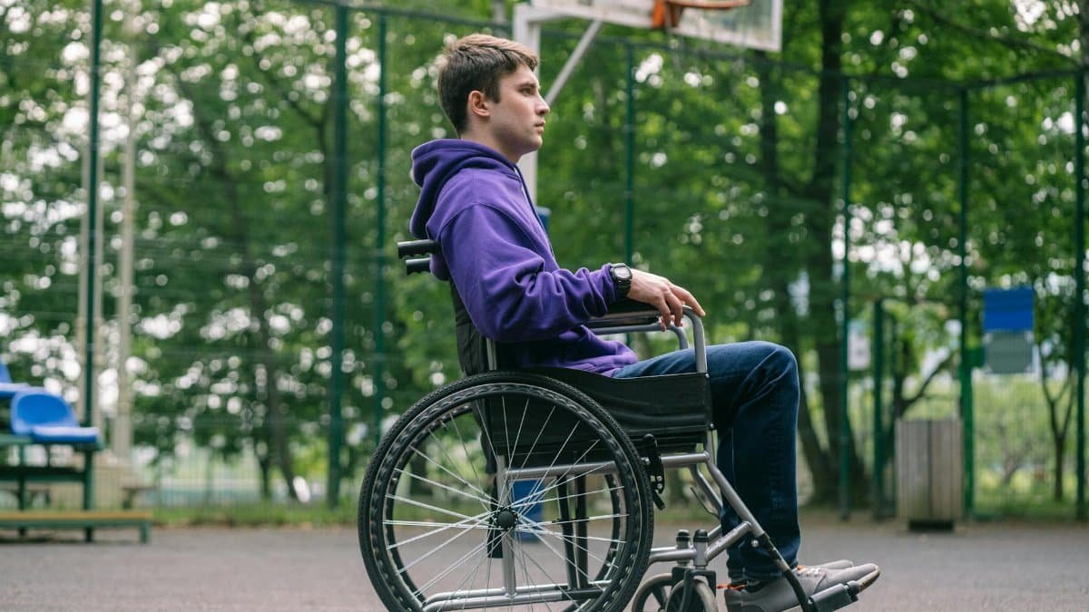 A young man in a purple hoodie sitting in a wheelchair on a basketball court.
