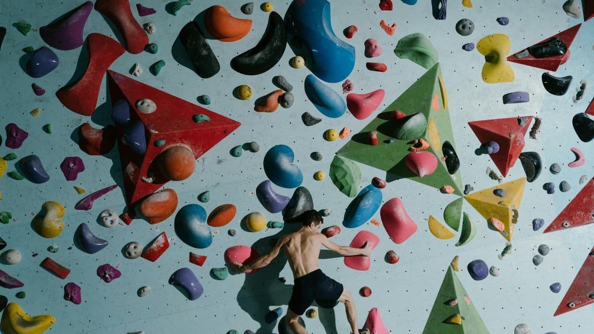 Man bouldering indoors on a colorful climbing wall, showcasing strength and agility.