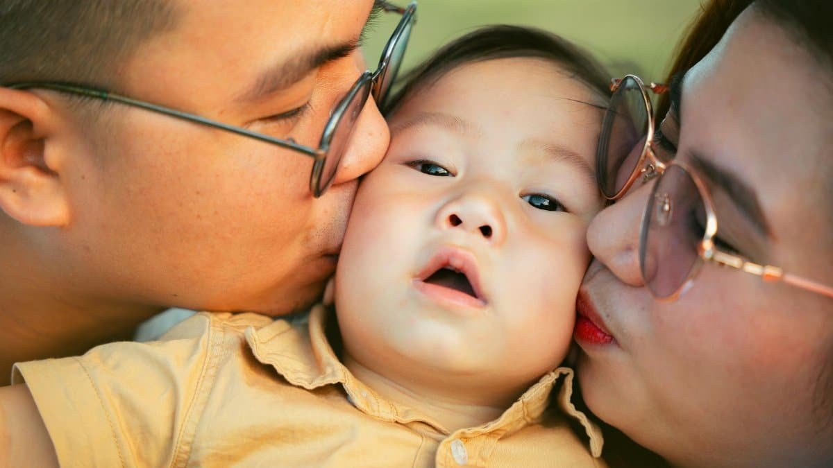 Close-up of affectionate parents kissing their baby, capturing a heartwarming family moment.
