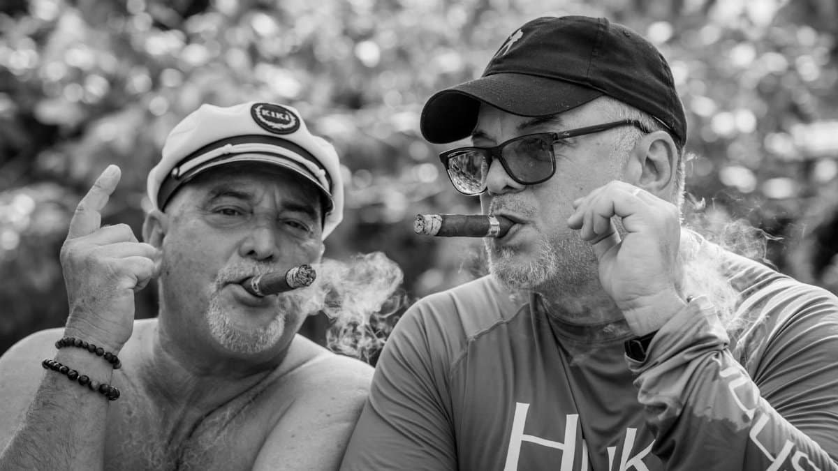 Two middle-aged men smoking cigars outdoors in Miami, captured in a candid black and white shot.
