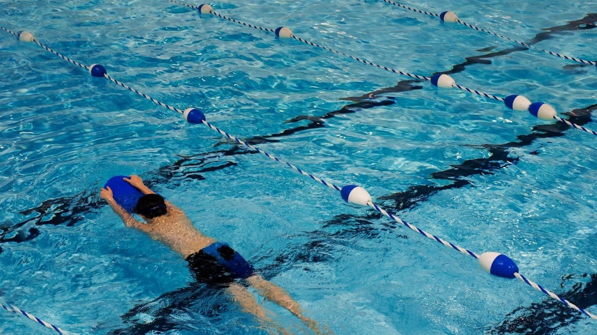 A young swimmer practicing with a kickboard in a swimming pool on a sunny day.