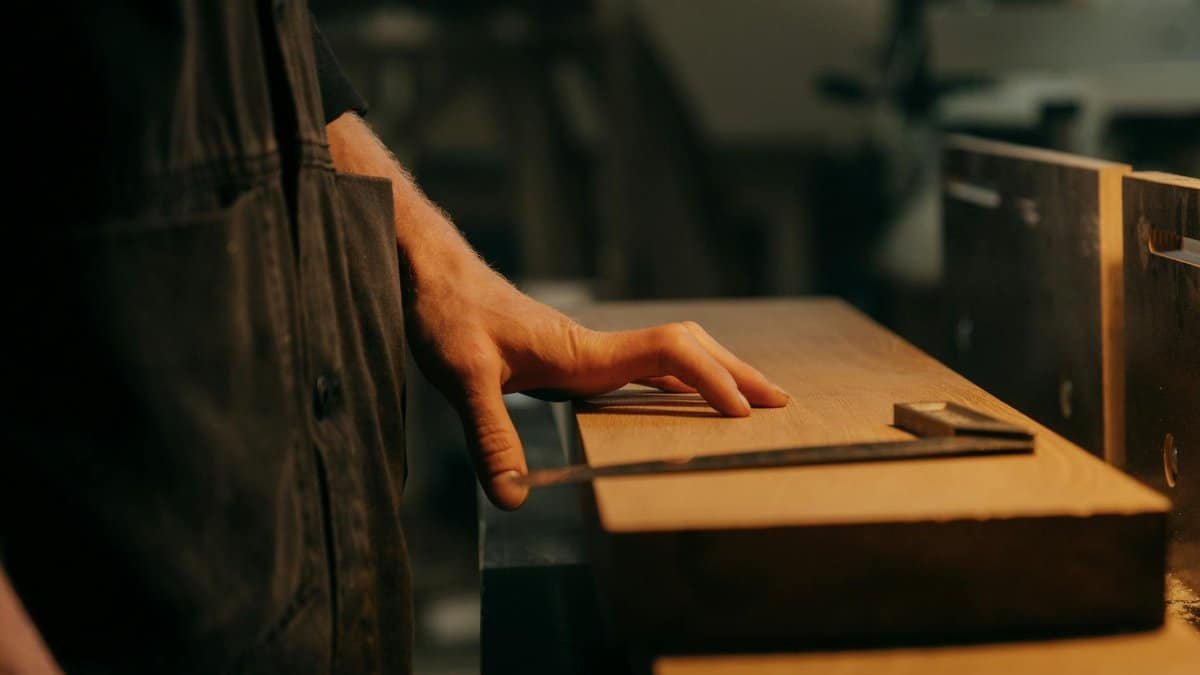 A craftsman measuring wood with precision tools in a workshop setting.