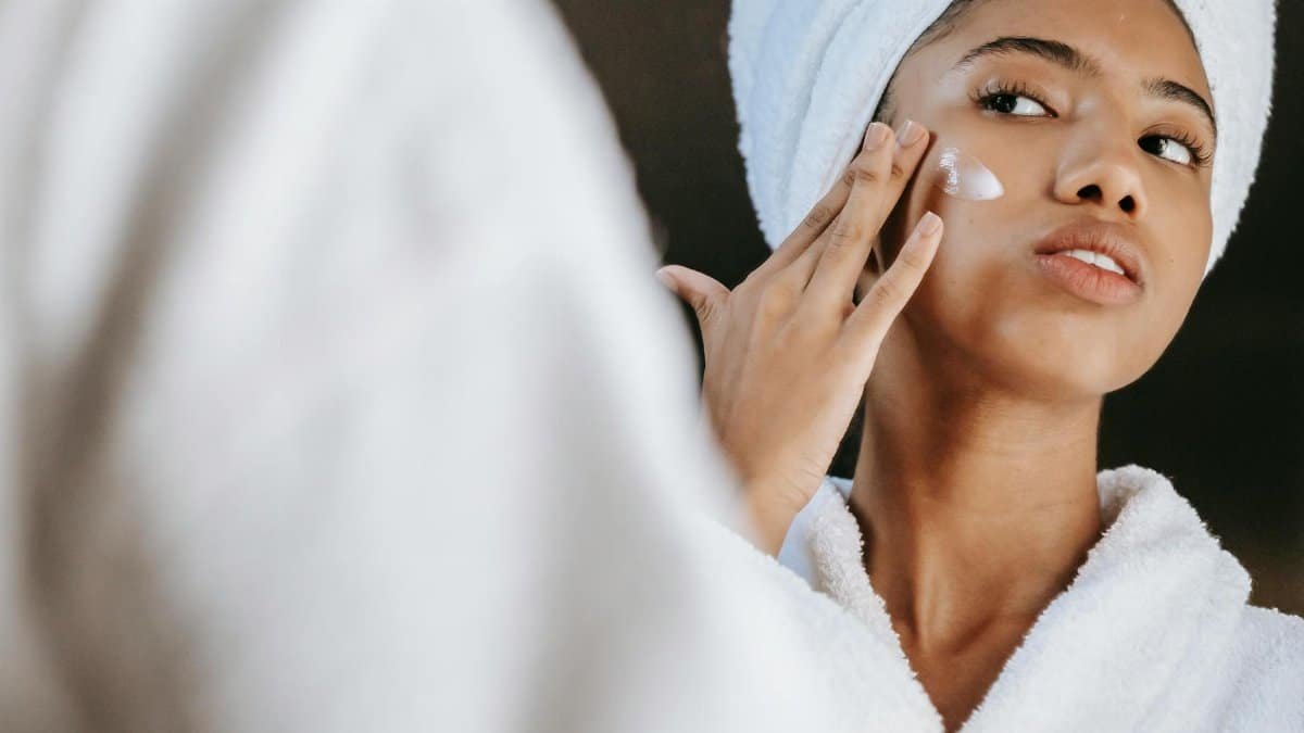 Woman in a bathrobe practices her skincare routine with moisturizing cream. Perfect for wellness themes.