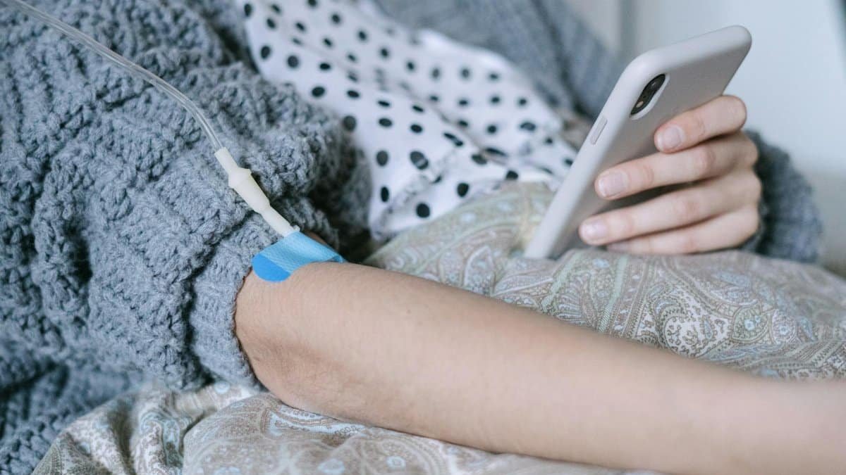 A woman receiving intravenous therapy for cancer treatment while using her phone, symbolizing connection and hope.