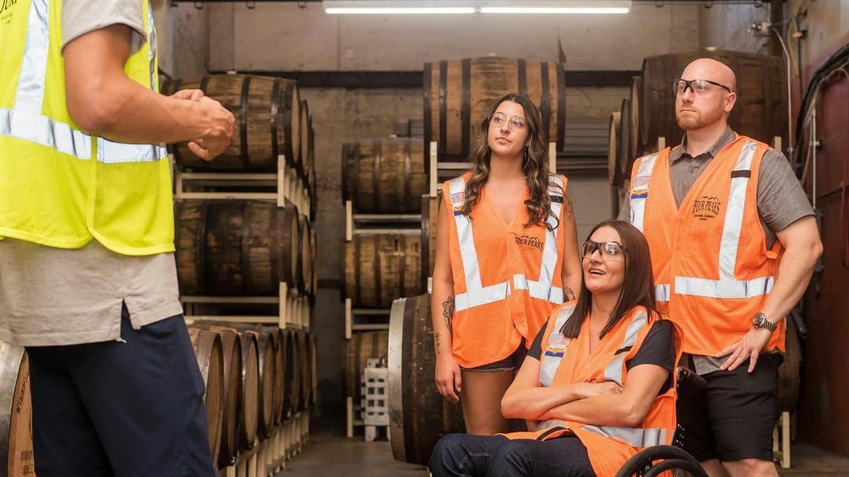 Group of adults in safety vests touring a brewery, highlighting inclusivity and accessibility.