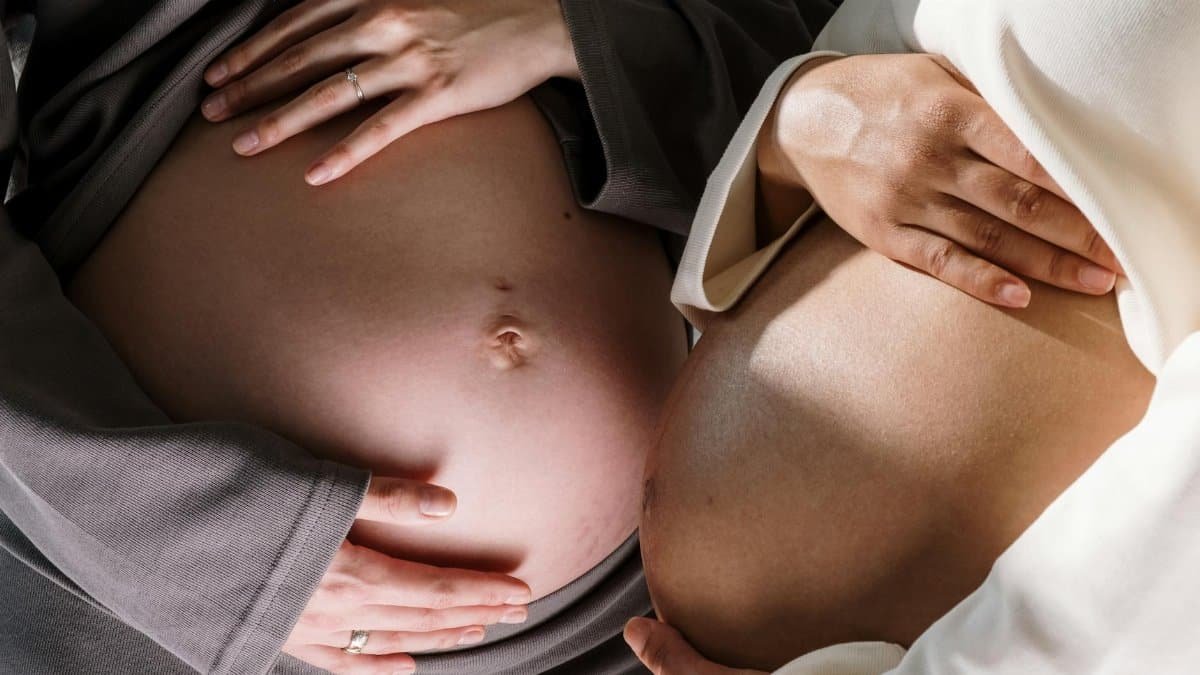 Two pregnant women gently touching their bellies, symbolizing togetherness in motherhood.