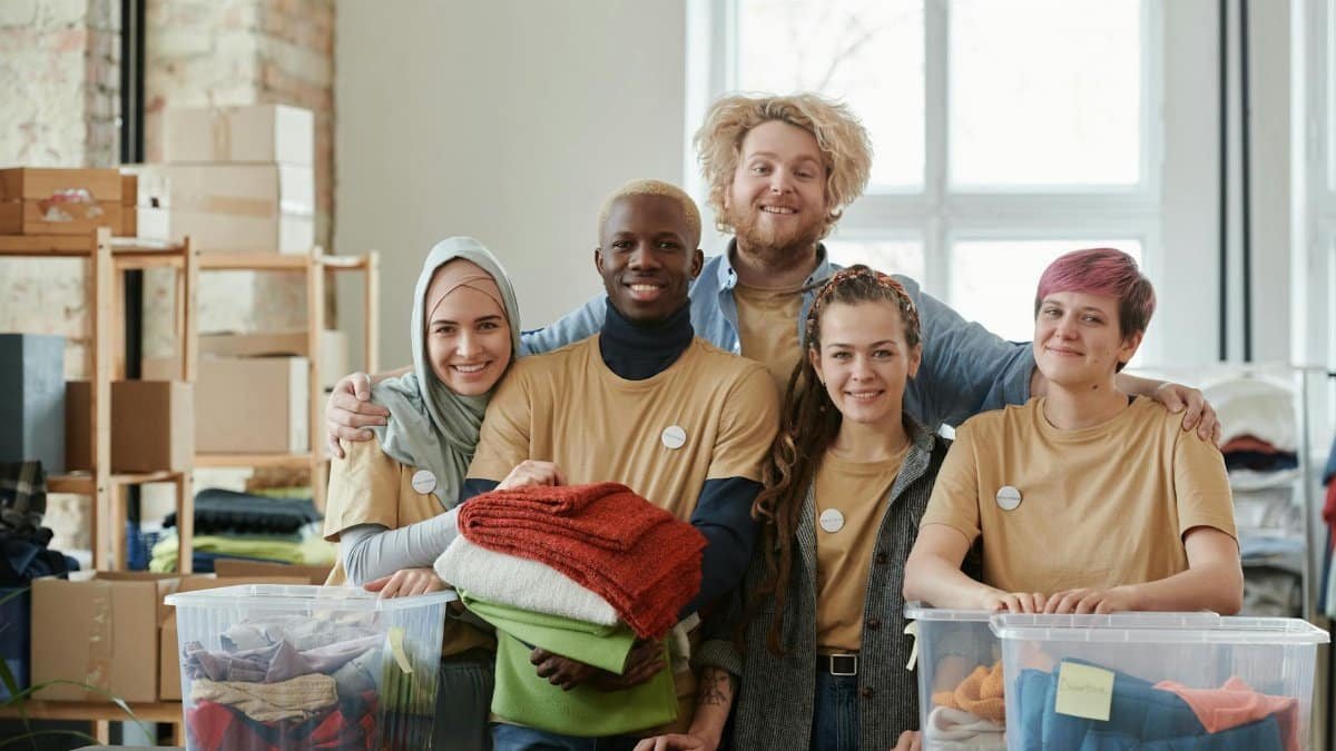 Group of diverse volunteers smiling while sorting clothes at a charity donation center.