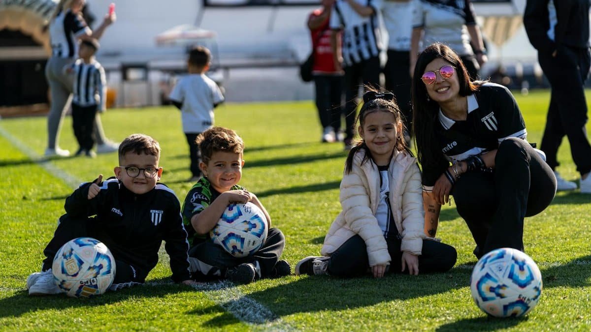 A group of happy children and their coach enjoy a sunny day on the football field.