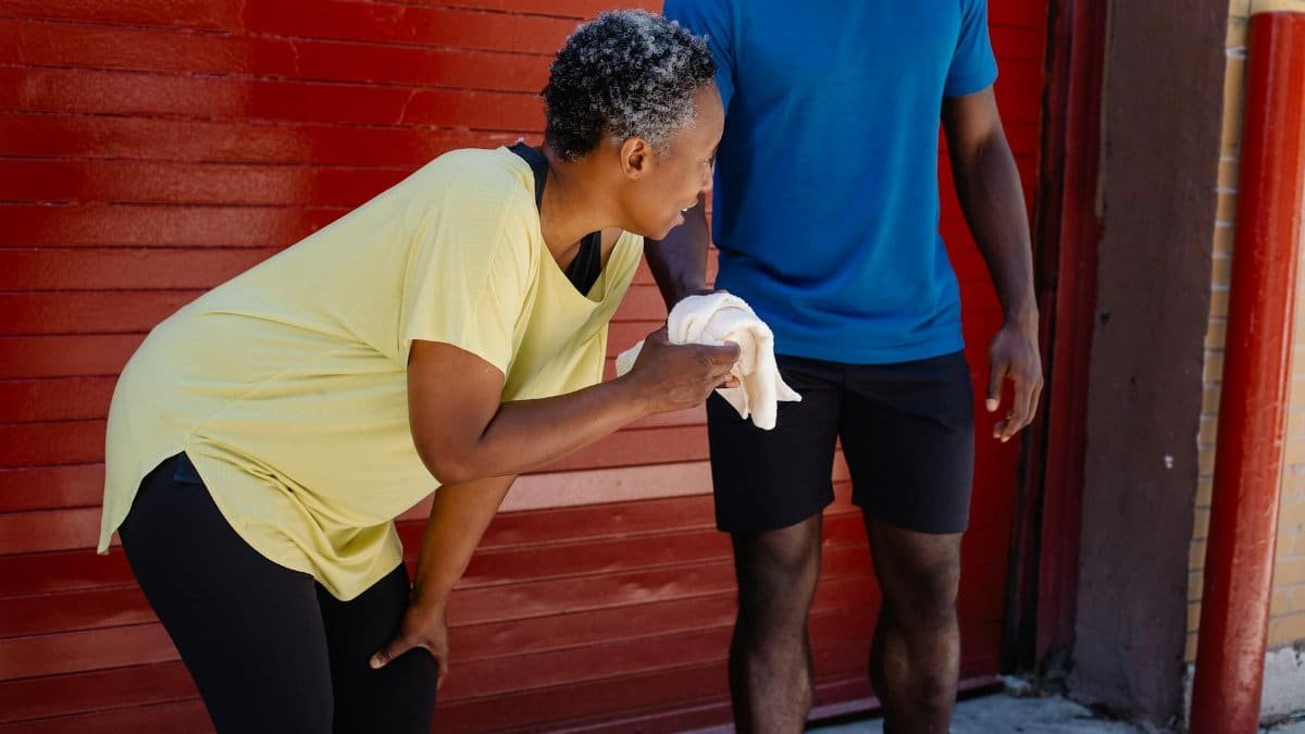 Two adults take a break after exercise against a red wall, embodying fitness and community.