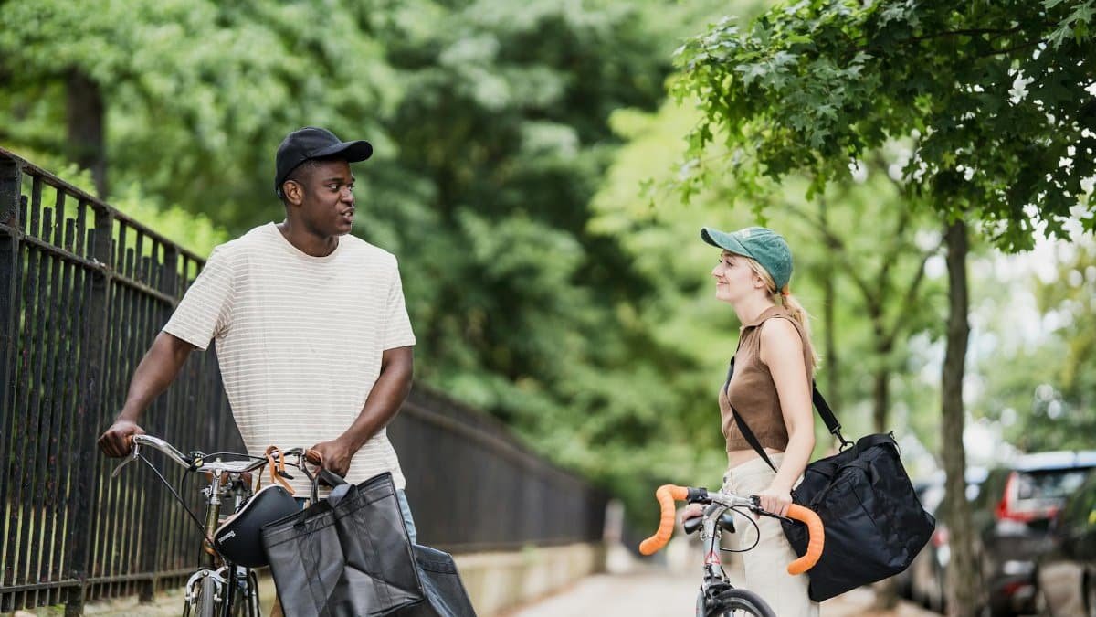 Two bicycle couriers with delivery bags chatting casually on a city street.