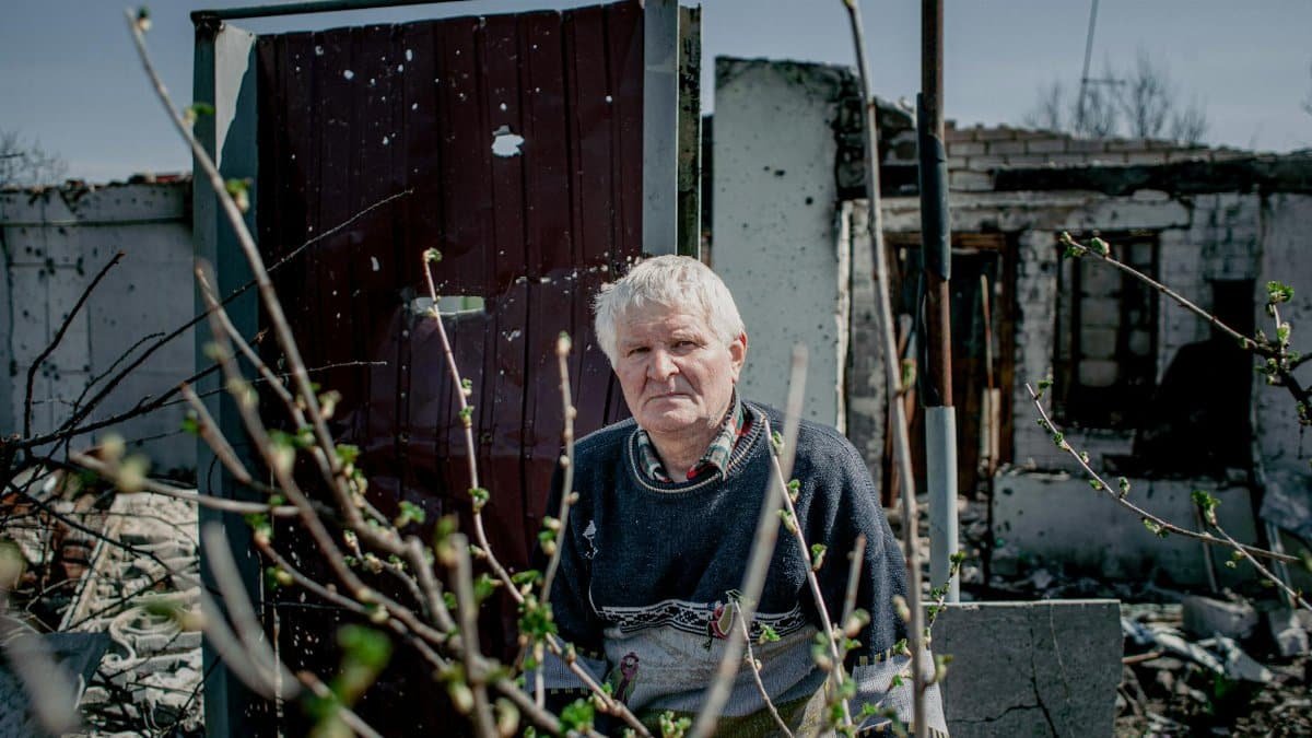 Portrait of an elderly man standing in a demolished Ukrainian village, symbolizing resilience.