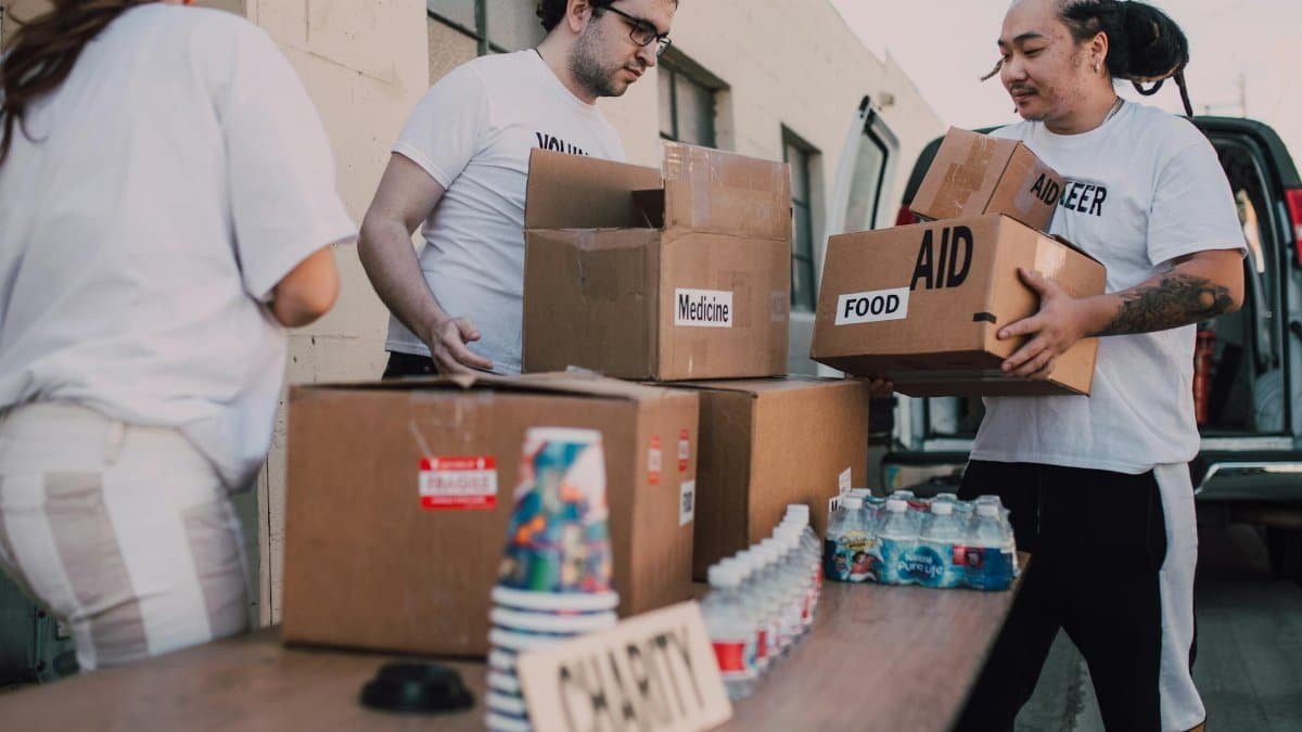 Volunteers loading aid boxes with food and medicine from a van outdoors.