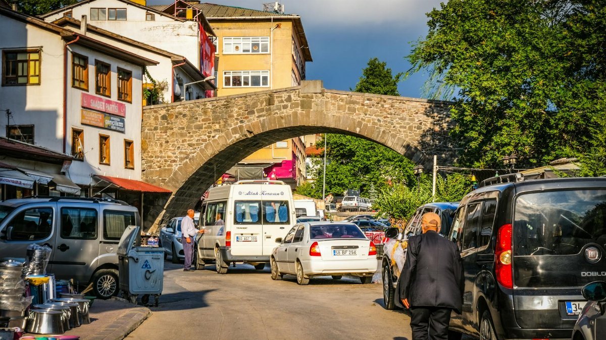 Lively urban street under a historic stone bridge, with people and cars