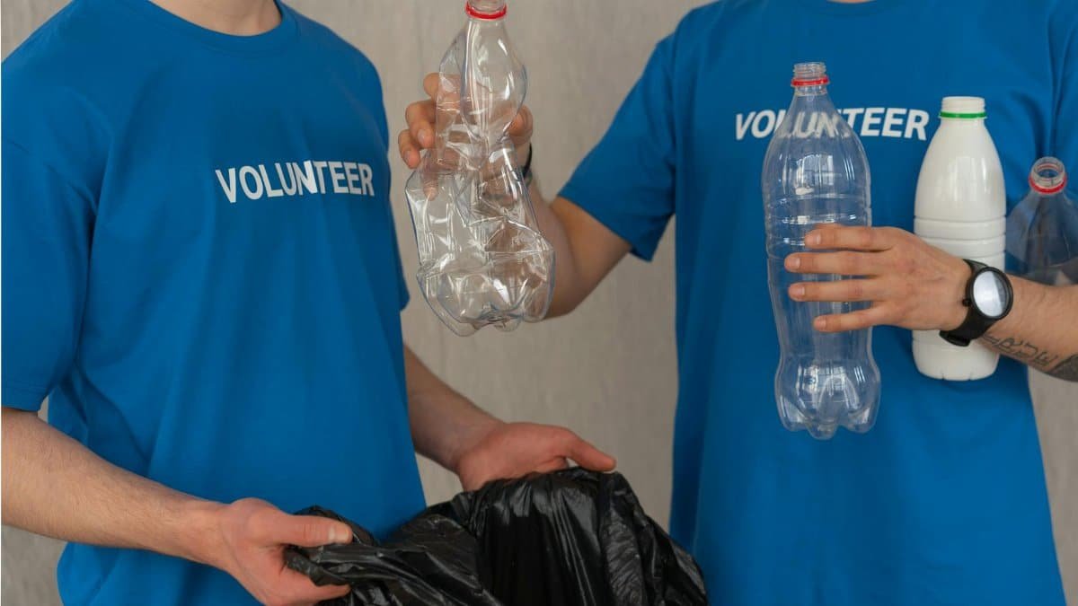Two volunteers in blue shirts collect plastic bottles for recycling, showcasing community involvement.