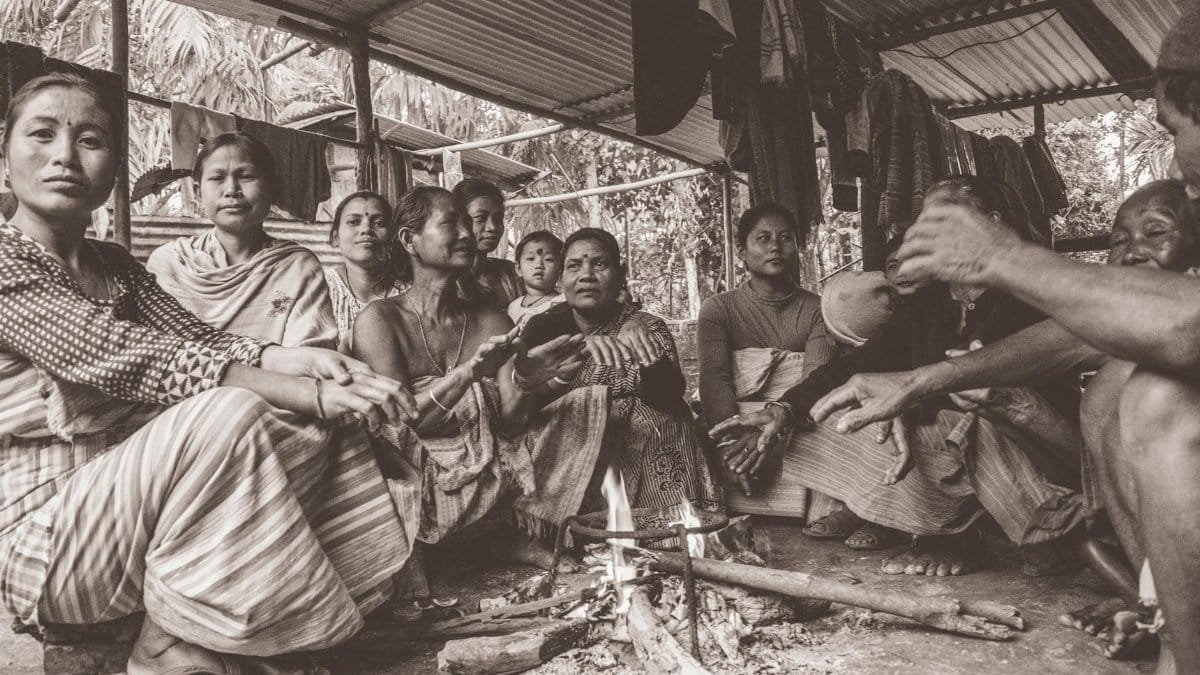 A tribal community gathered indoors in Assam. Captured in warm grayscale, it showcases their culture and traditions.
