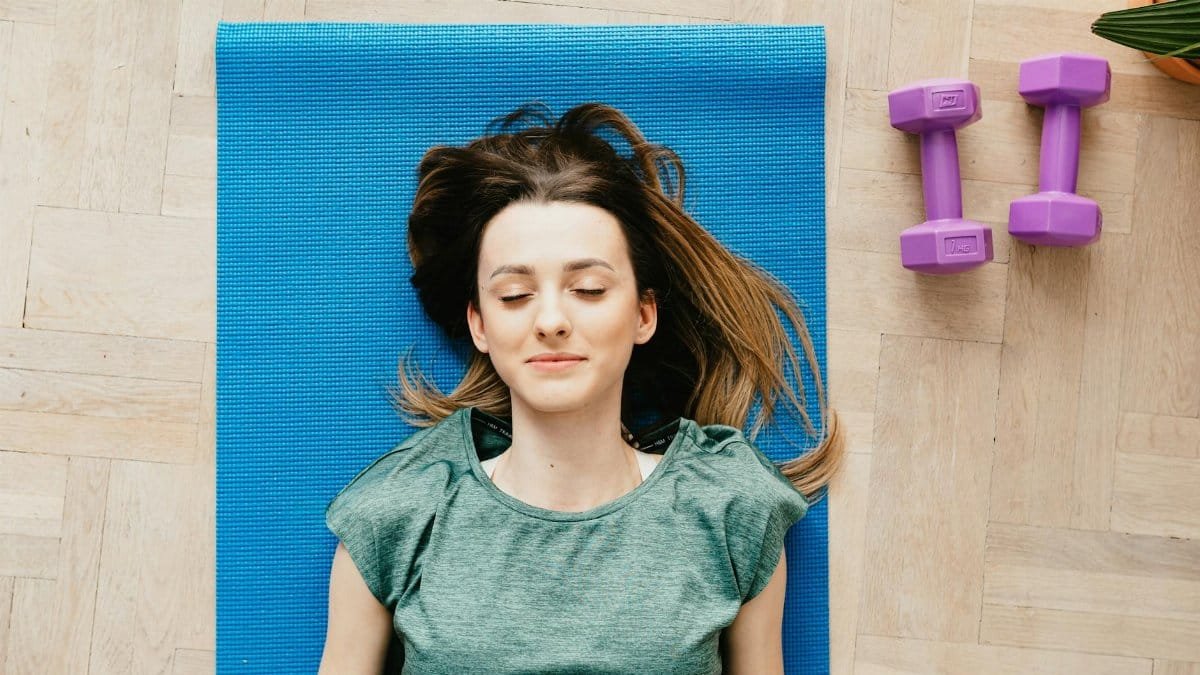 A young woman peacefully resting on a yoga mat with dumbbells beside her indoors.