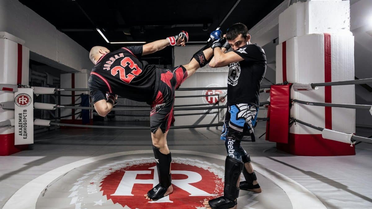 Two male athletes practice kickboxing techniques indoors in a training ring.
