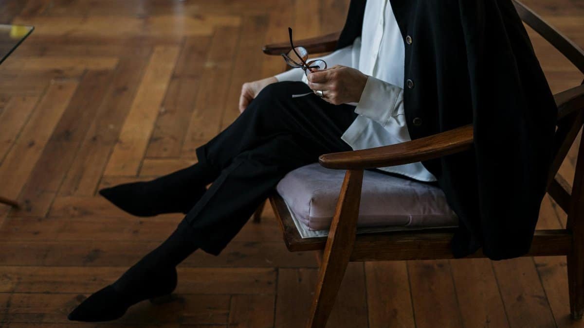 A woman holding glasses, seated indoors, exuding professionalism and calm.