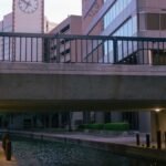 Scenic view of canal under modern bridge with clock tower and buildings in Irving, TX.
