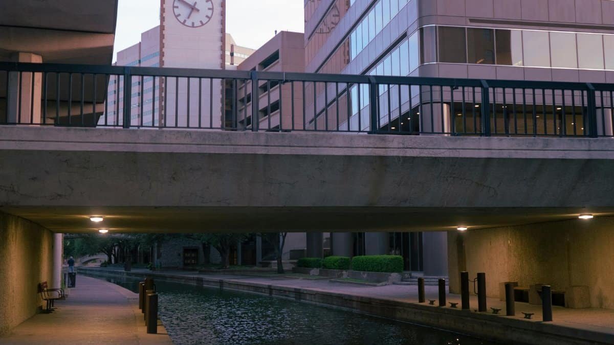 Scenic view of canal under modern bridge with clock tower and buildings in Irving, TX.