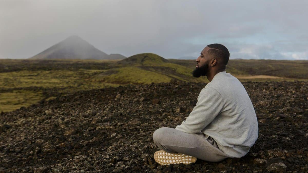 Man meditating on rocky terrain with mountain backdrop. Peace and tranquility outdoors.