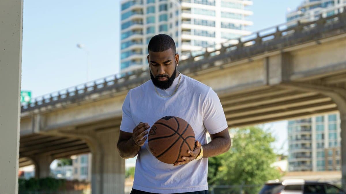 A man holding a basketball under a city bridge, conveying focus and urban sports atmosphere.