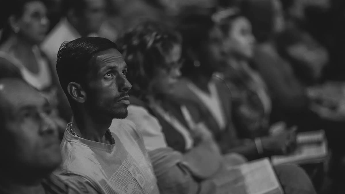 A monochrome photograph of a focused man in a diverse audience setting.