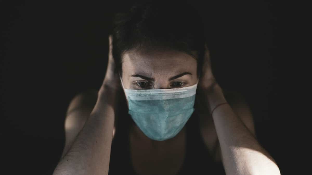 Adult woman wearing a face mask in a dark setting, expressing stress or worry.