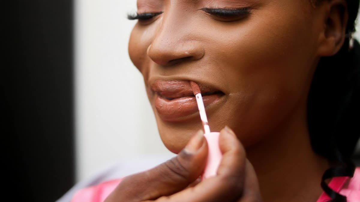 Close-up of a woman applying lip gloss, enhancing natural beauty with a subtle makeup style.