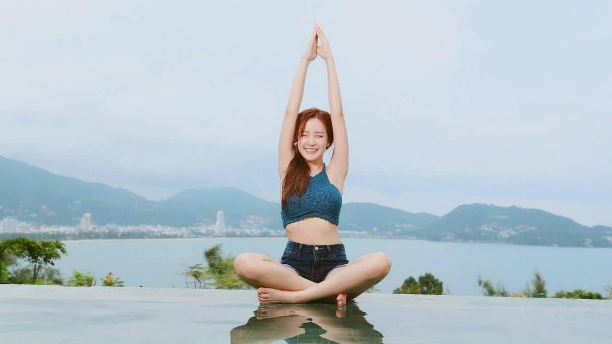 Young woman doing yoga by a scenic waterfront, enjoying a serene landscape.