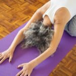 Elderly woman performing yoga pose on a purple mat, promoting wellness and relaxation.