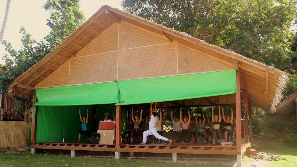 Group yoga session in a bamboo pavilion in Thailand, demonstrating warrior pose for well-being.