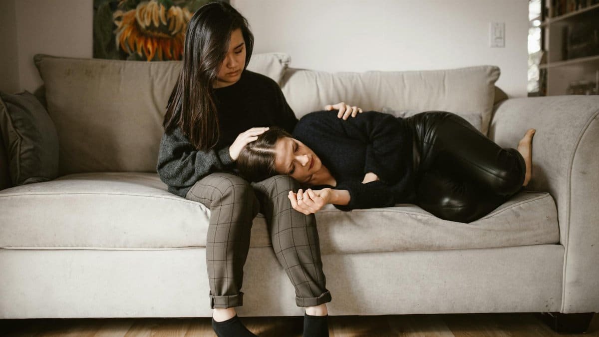 A comforting scene of empathy and support between two women sitting on a sofa indoors.