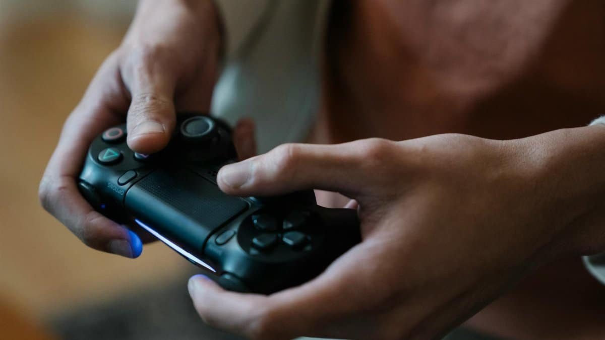 Hands gripping a black game controller indoors, capturing a moment of focused gaming.