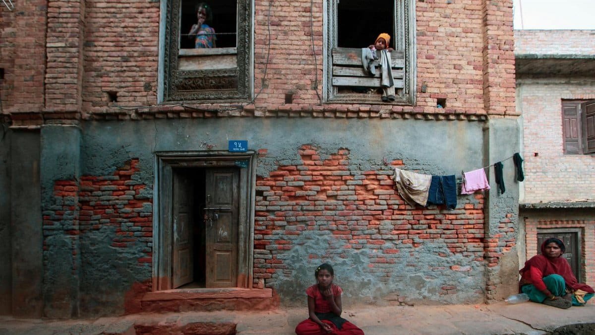 A rustic brick house with residents visible in the windows and doorway, showcasing a quaint urban scene.