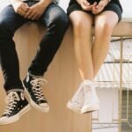 A relaxed couple sitting on a ledge, wearing stylish sneakers, showcasing togetherness.