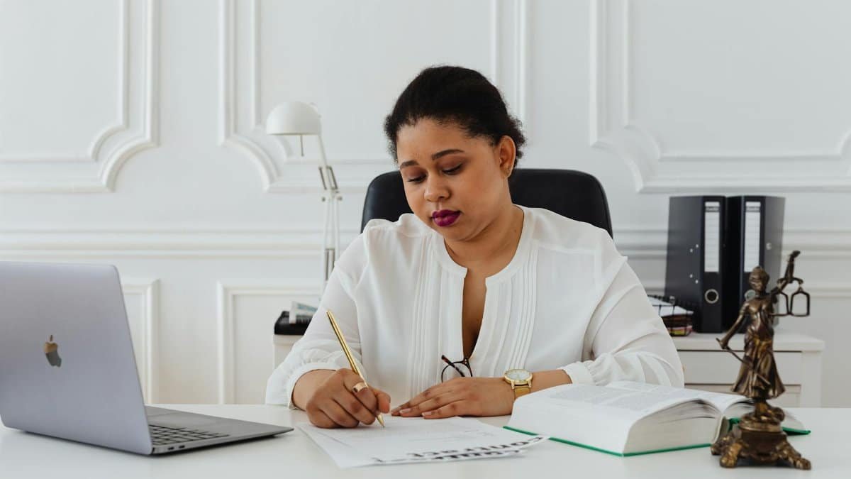 African American woman lawyer signing documents at a desk, symbolizing professionalism.