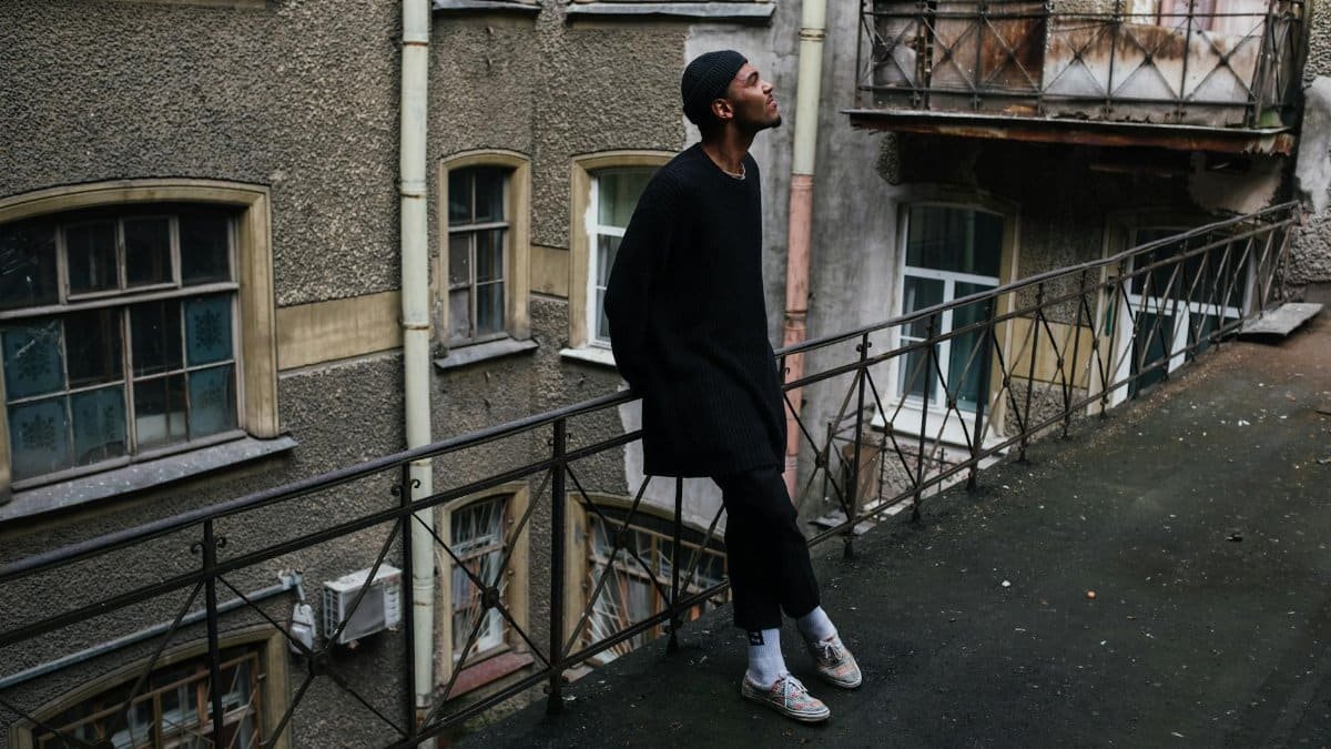 A man stands on a deteriorating balcony in an urban area with vintage architecture.