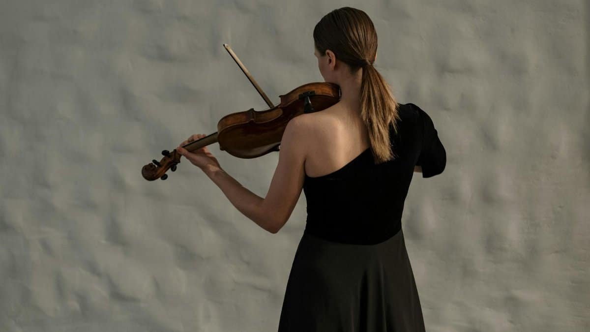 Professional female violinist in a black dress captivatingly plays indoors, focusing on her craft.
